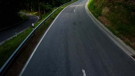 shot-from-a-drone-flying-low-over-the-ground-on-a-car-driving-along-the-road-in-a-green-forest-in-summer