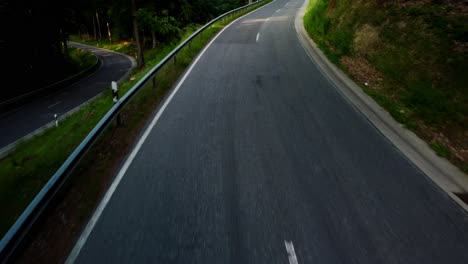 shot from a drone flying low over the ground on a car driving along the road in a green forest in summer