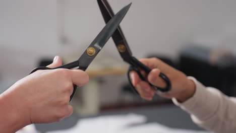 Close up of hands holding sewing clipper engaging in playful scissors cutting fight above work table filled with colorful fabric samples in bright creative workspace full of energy