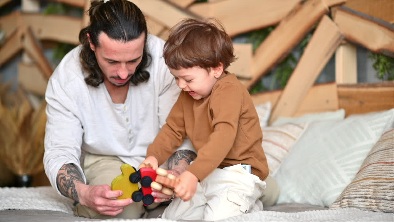 Father playing with his son with colourful, ecological wooden toys on the bed