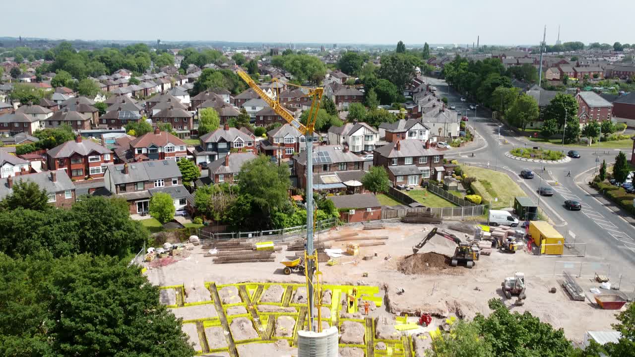 Tall crane setting building foundation in British town neighbourhood aerial view tilt down over suburban townhouse rooftops