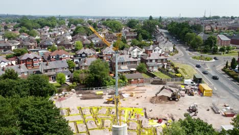 tall crane setting building foundation in british town neighbourhood aerial view tilt down over suburban townhouse rooftops