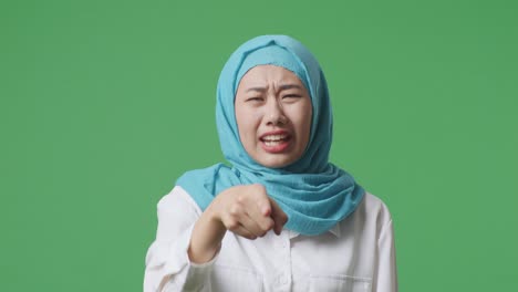 close up of asian muslim woman shouting at camera while standing in the green screen background studio