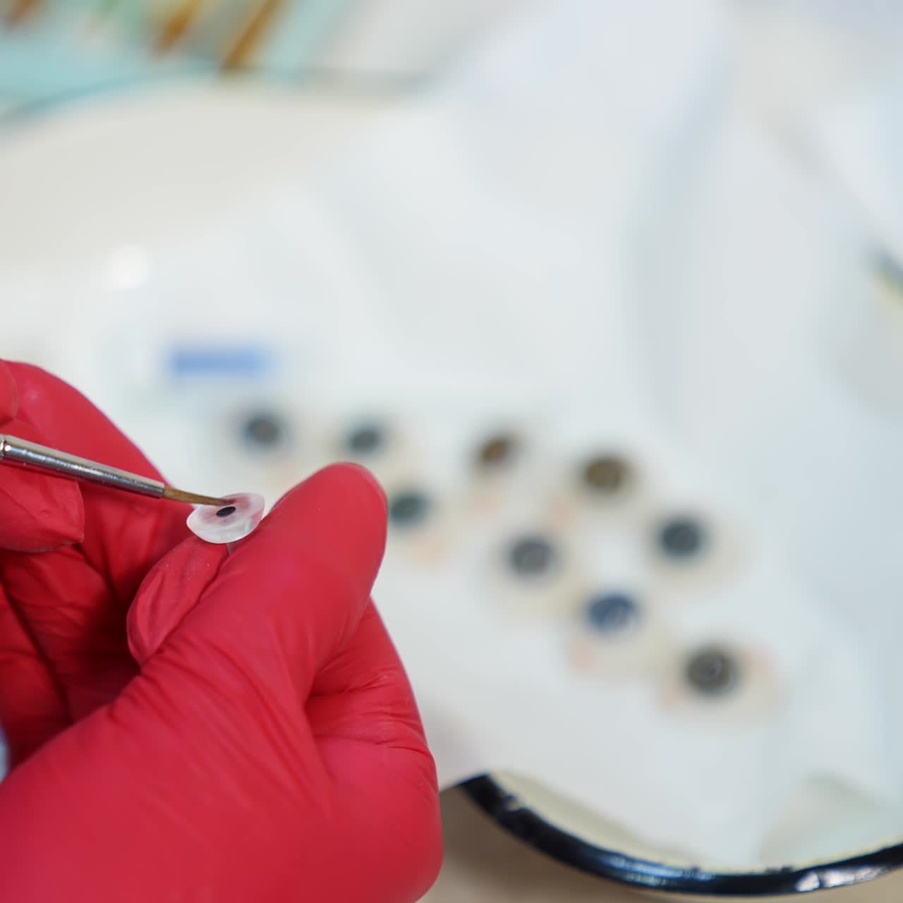 Few eye prosthesis in medical bowl. Medical specialist in red gloves painting artificial eye in the laboratory. Close-up