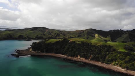 Aerial-view-of-mountains-surrounded-by-clear-ocean-water-in-Kereta-Coromandel-New-Zealand,-Orbit-Shot