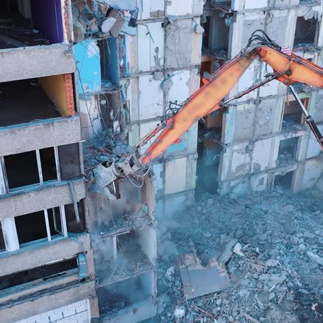 ruined building is being demolished with the help of special machinery. big claw is ruining the floors of the wrecked building. debris falling and dust raising