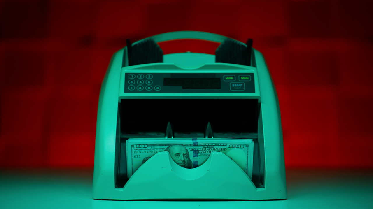 Counting machine flipping dollars in neon light closeup. Currency exchange bills