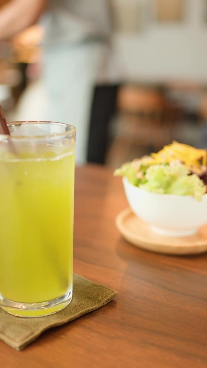 Camarero coloca té verde y ensalada en mesa de madera en cafetería luminosa, informal y con luz natural