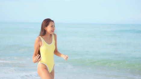 노란색 수영복을 입은 아름다운 여성이 해변을 산책합니다.
