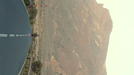 vertical shot, young man runs on long road with volcano landscape in background