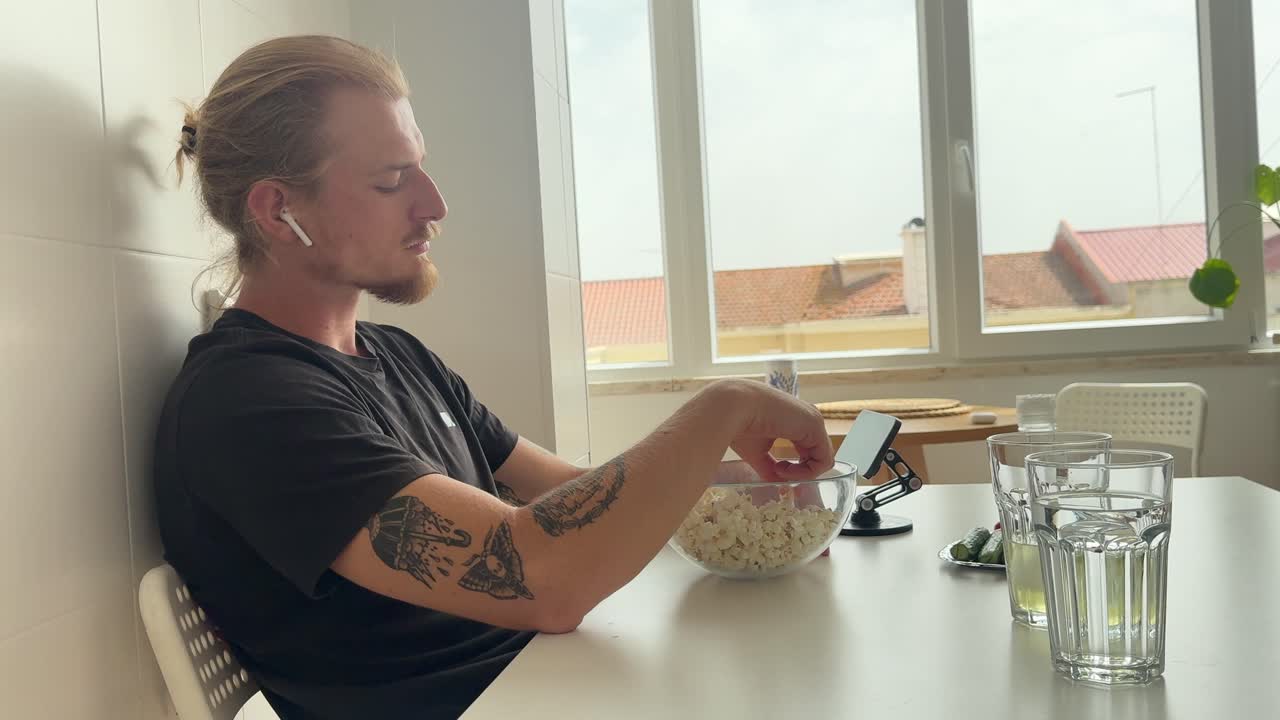Ung mand spiser popcorn og ser video på telefonen