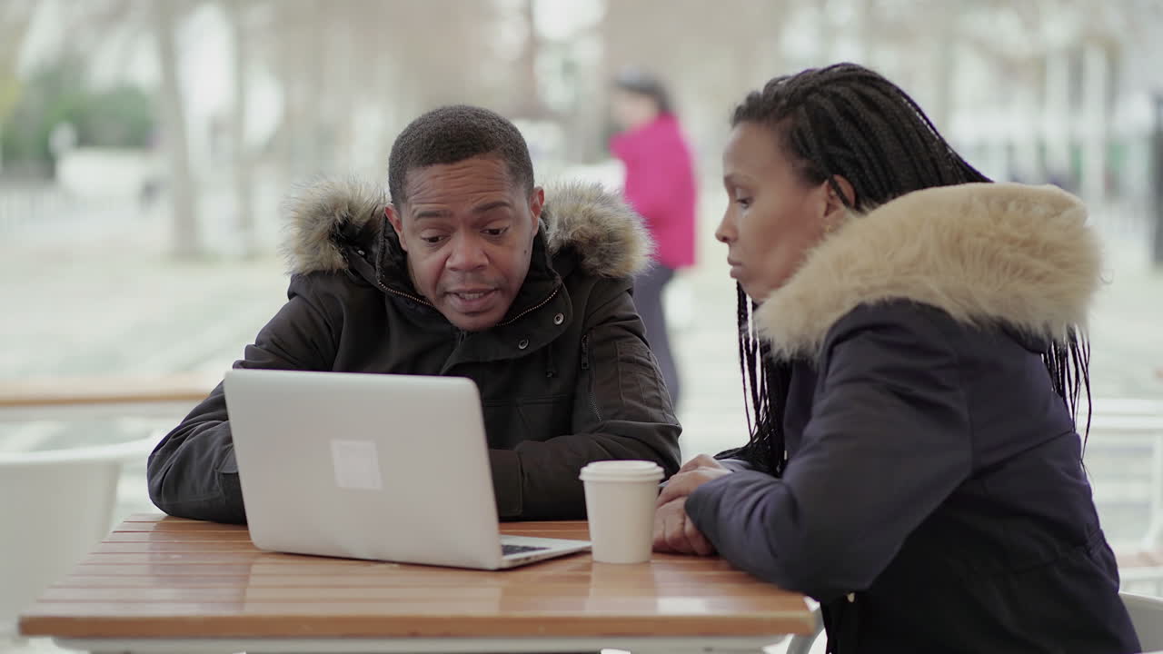 Afro-American middle-aged man in black jacket with fur hood explaining data to Afro-American young girl with braids