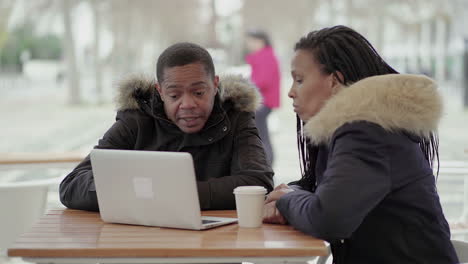 afro-american middle-aged man in black jacket with fur hood explaining data to afro-american young girl with braids