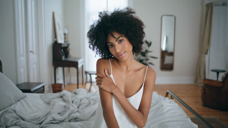 retrato mujer serena sentada en la cama. mujer morena rizada tocando la piel suave posando