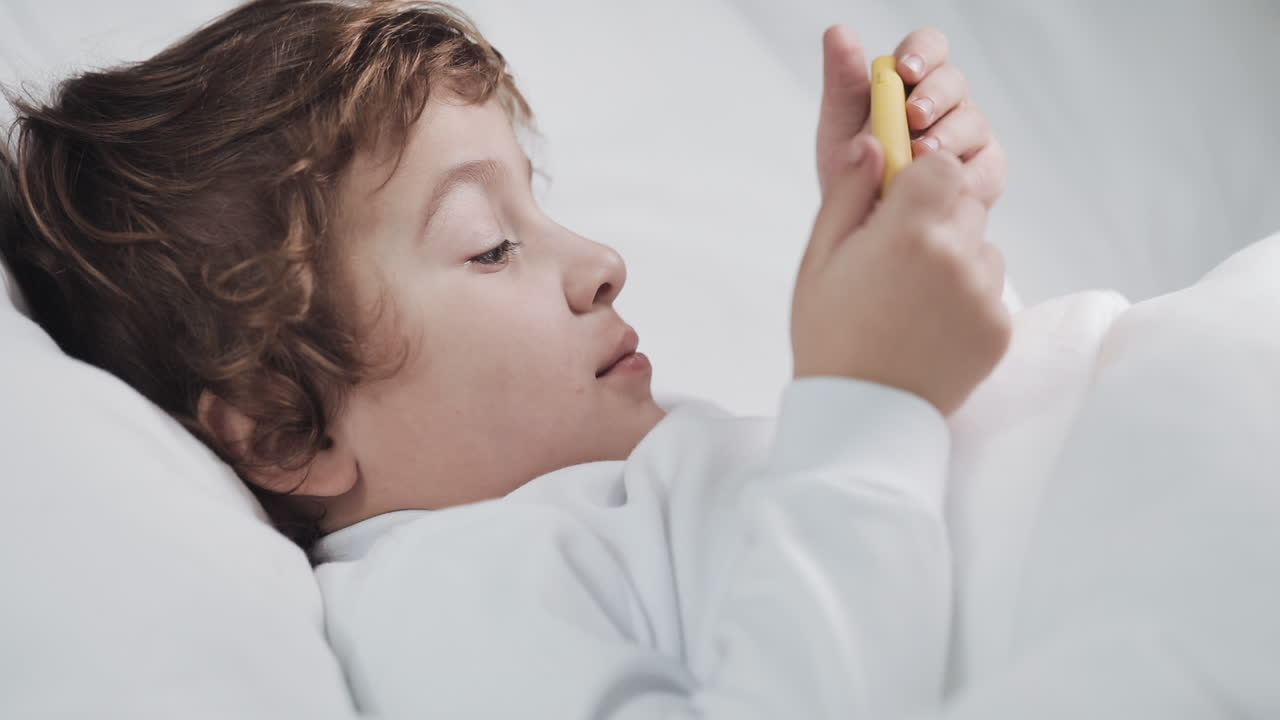 Boy Using Mobile Phone in Bed