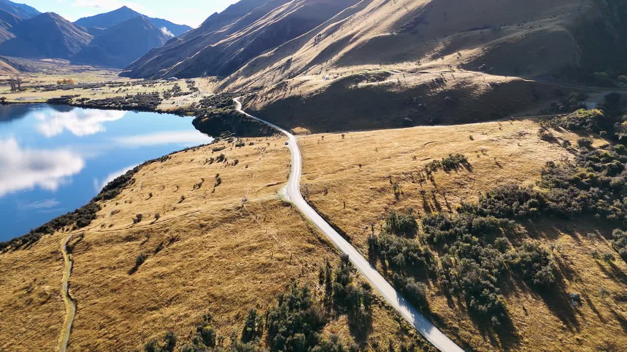 Aerial footage captures Lake Moke's serene landscape in Queenstown, New Zealand, with winding roads and reflective waters under clear skies