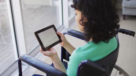 Thoughtful-biracial-disabled-woman-in-wheelchair-using-tablet-in-living-room,-copy-space-on-screen