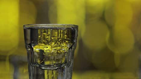 Barman-pour-frozen-vodka-from-bottle-into-shot-glass-against-shiny-gold-party-background.-Close-up