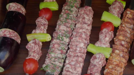 close-up shot of raw shish kebab skewers with eggplant, tomato, and green pepper on a wooden board.