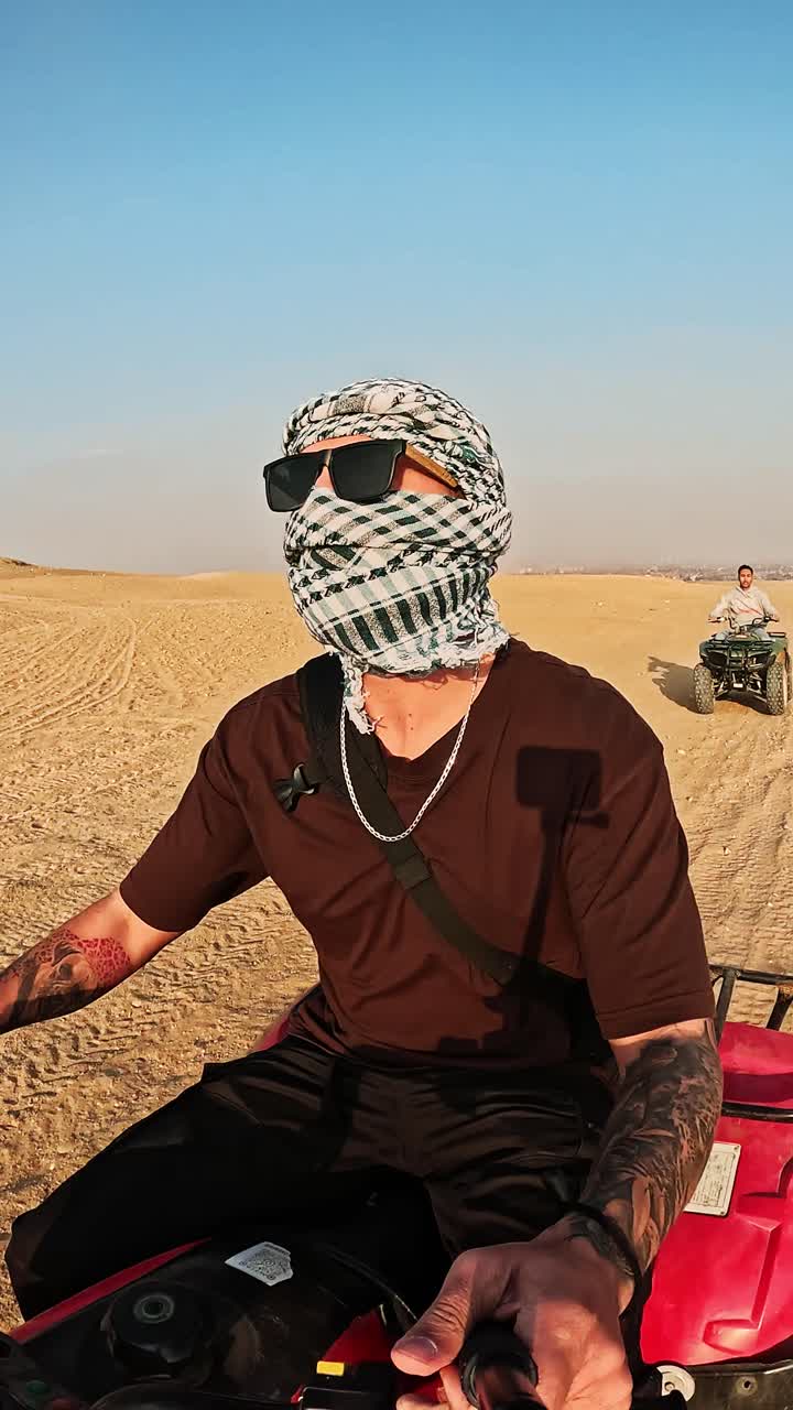 Uomo con Keffiyeh e occhiali da sole alla guida di un quad nel deserto