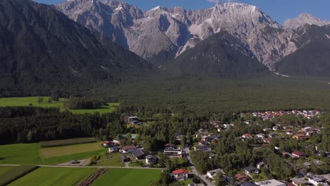 drone approaching alps in austria on a sunny day with blue skies and little clouds and villages and houses in the woods