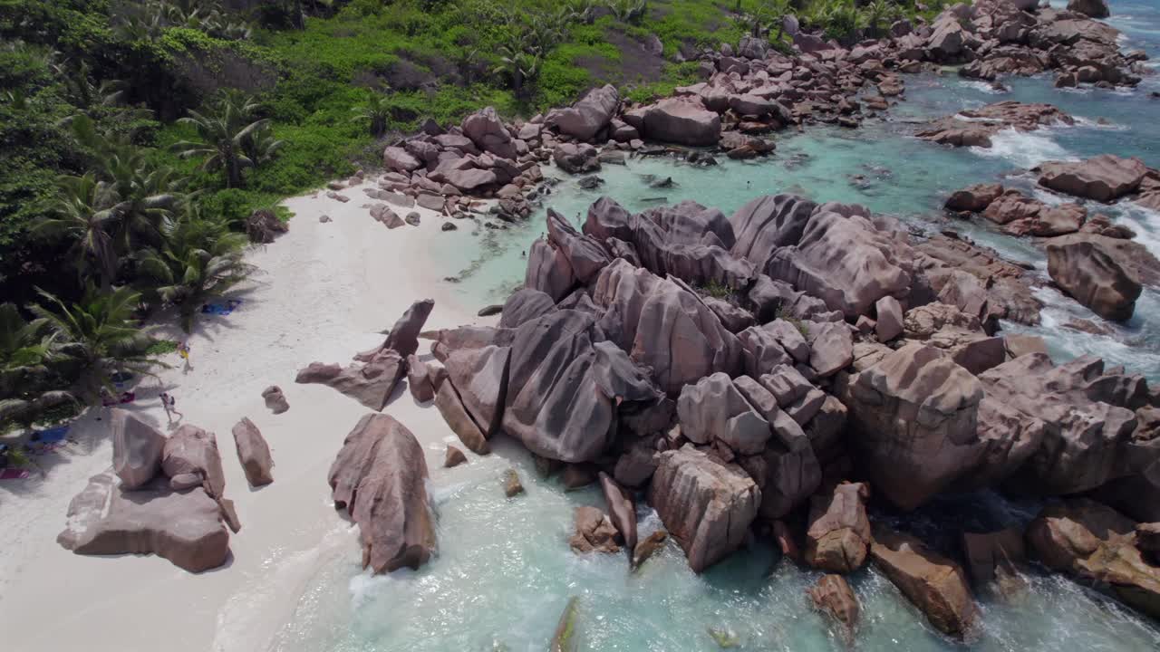 Pemandangan Drone Mata Burung yang Bergerak Turun dan Miring dari Batu Granit Dekat Garis Pantai, Air Pirus Jernih, Pantai Berpasir Putih, Orang-orang Snorkeling, Pohon-pohon Dekat Pantai, Anse Cocos, La Digue, Seychelles 009