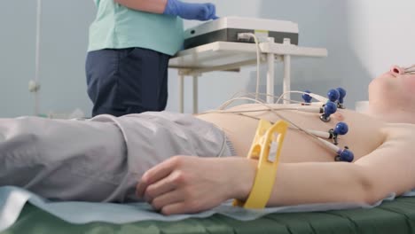 examen cardíaco en un hospital con un cardiógrafo profesional. el paciente se acuesta en una cama con sensores conectados.