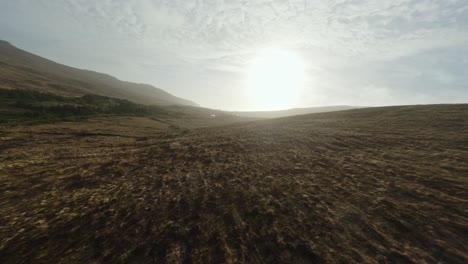 drone flying towards the sunset above a brown hill in ireland