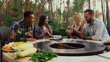 young people discussing food preparation outside. friends sitting near bbq grill