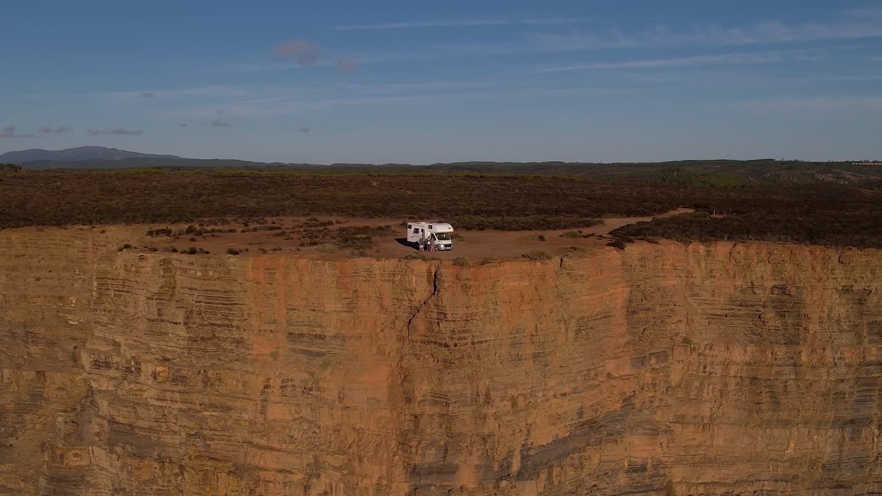 Autocaravana en el borde de un acantilado de las Falésias da Arriba Fóssil en Costa da Caparica, Almada, Portugal, sobre un muro sedimentario atlántico estratificado, dron alejándose y efecto de profundidad de paralaje