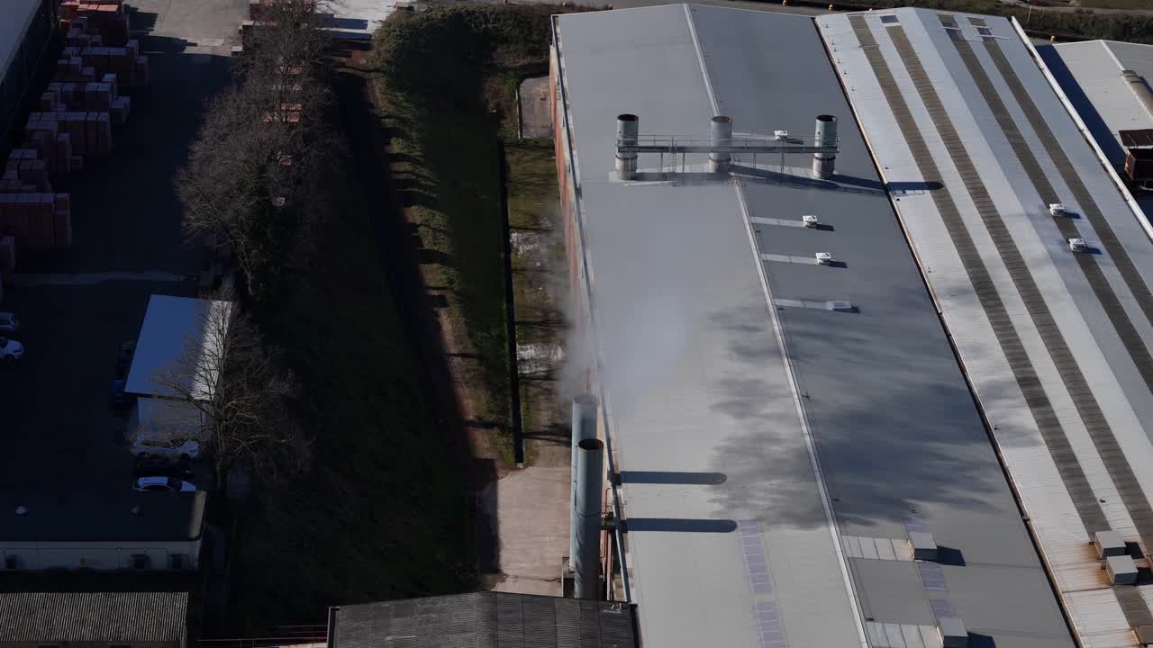 Industriskorstene udleder hvid damp ved siden af store fabriksbygninger og lagerbygningstage inden for et produktionskompleks