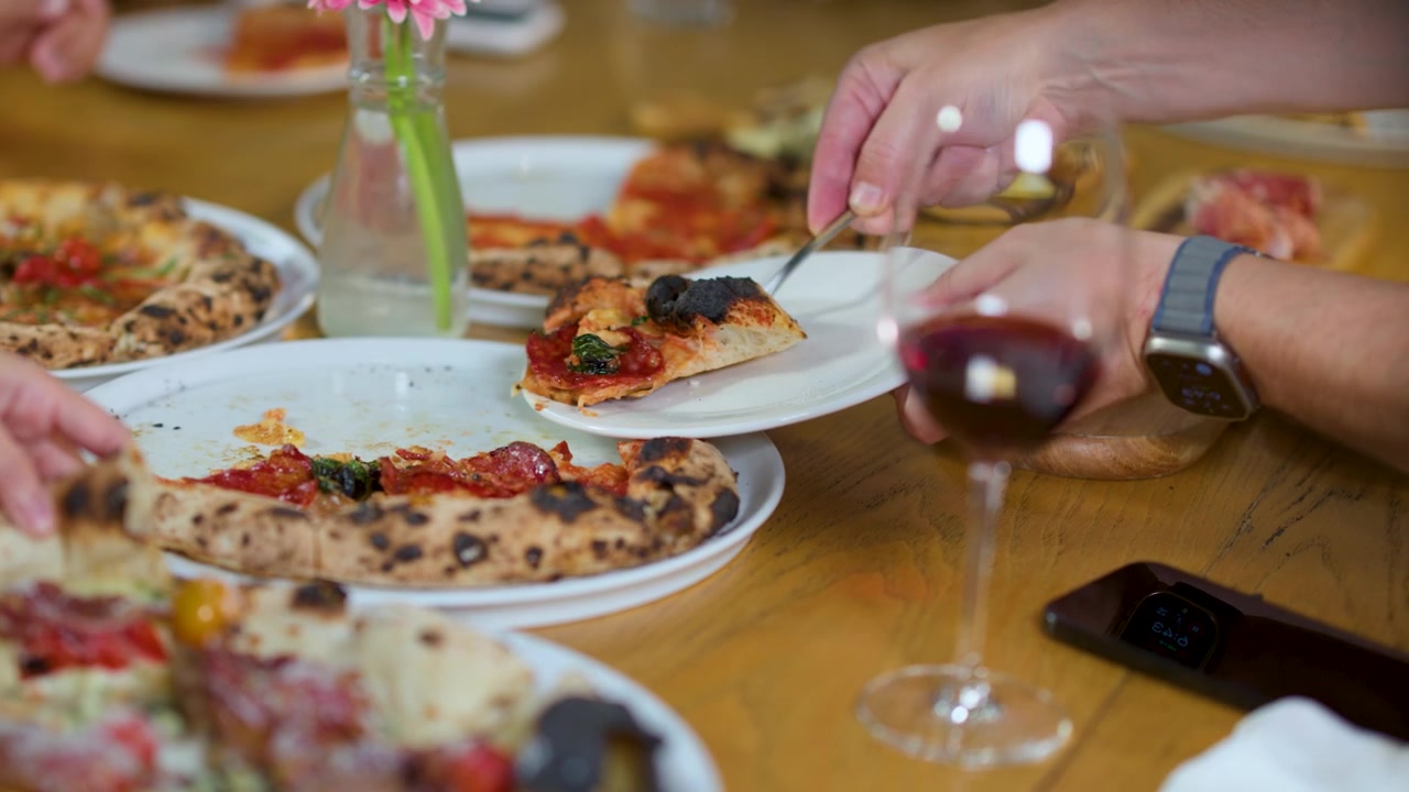Primo piano di mani che servono fette di pizza al salame piccante sui piatti durante una cena di gruppo