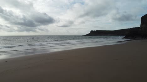 Playa-Aérea-En-Rápido-Movimiento-Tomada-Con-Pequeñas-Olas-Y-Un-Espectacular-Paisaje-Nublado-En-La-Bahía-De-Mewslade,-Gales,-Reino-Unido-4k