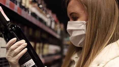 young woman in medical mask selects wine in supermarket buying products during pandemic coronavirus