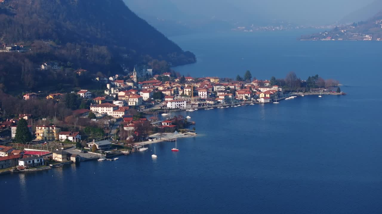 Pella village on shores of Lake Orta, Italy, hazy sky, colorful buildings, boats, ideal for travel, Italian lakes scenery. Aerial drone ascending, copy space