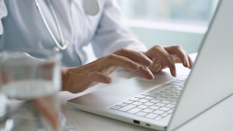 close-up view of senior caucasian female doctor hands typing on laptop at desktop