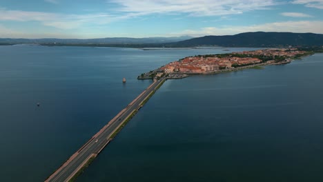 Coches-En-La-Carretera-Del-Puente-Que-Cruza-La-Laguna-Hacia-La-Ciudad-De-La-Isla-Orbetello-Cerca-Del-Monte-Argentario-Y-El-Parque-Natural-Maremma-En-Toscana,-Italia,-Con-Reflejos-En-El-Agua