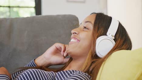 una feliz adolescente biracial con auriculares sonriendo en casa, en cámara lenta