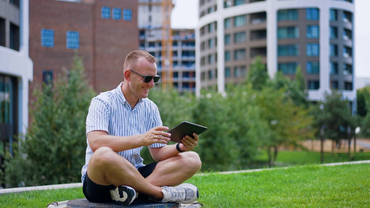 Man sitting with tablet. Person sits crossed legs on round base in park looking at digital screen.