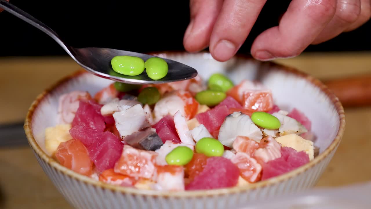 Primo piano di uno chef che sistema gli edamame su una vivace ciotola di chirashi sushi con illuminazione calda da ristorante