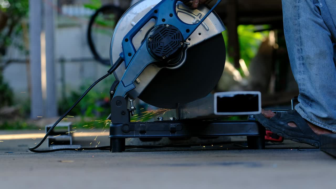 trabajador cortando tubos de acero metálico usando una sierra de corte circular con luz brillante.