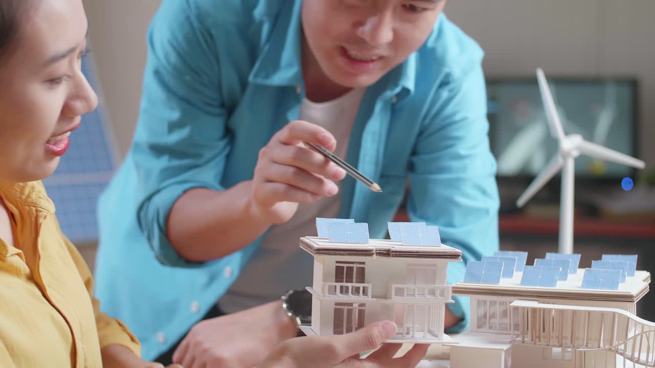 태양 전지 패널이 있는 작은 집의 모형을 만드는 데 서로 도움을 주는 아시아인 남녀의 클로즈업
