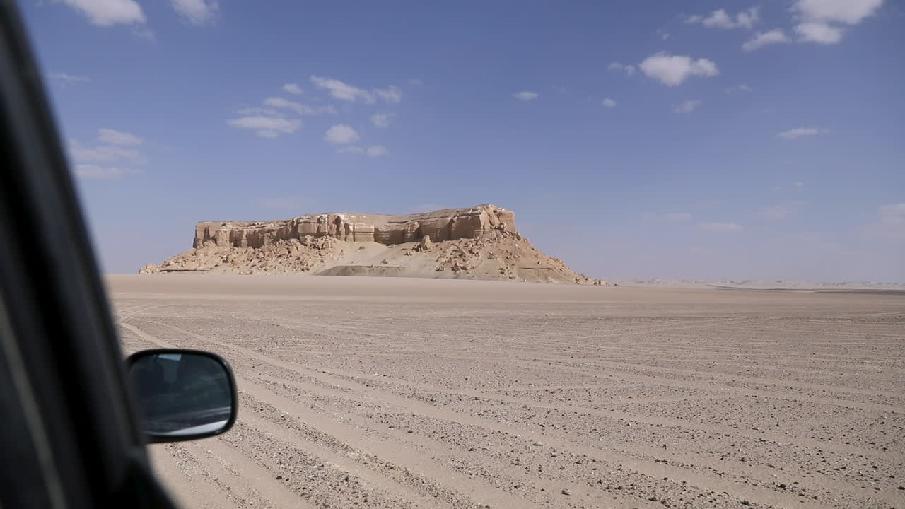 A car walking in the desert in front of a large mountain - long shot