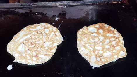 two omelettes being flipped on a cast iron pan with spatula