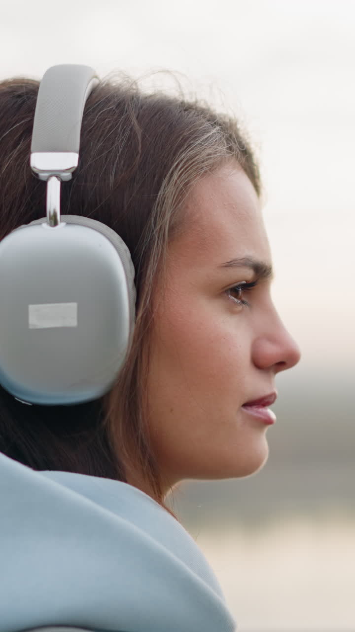 Close-up side view of young woman walking while listening to music with headphones on, focusing on her surroundings, calm, peaceful walk in an outdoor environment with focus on her expression