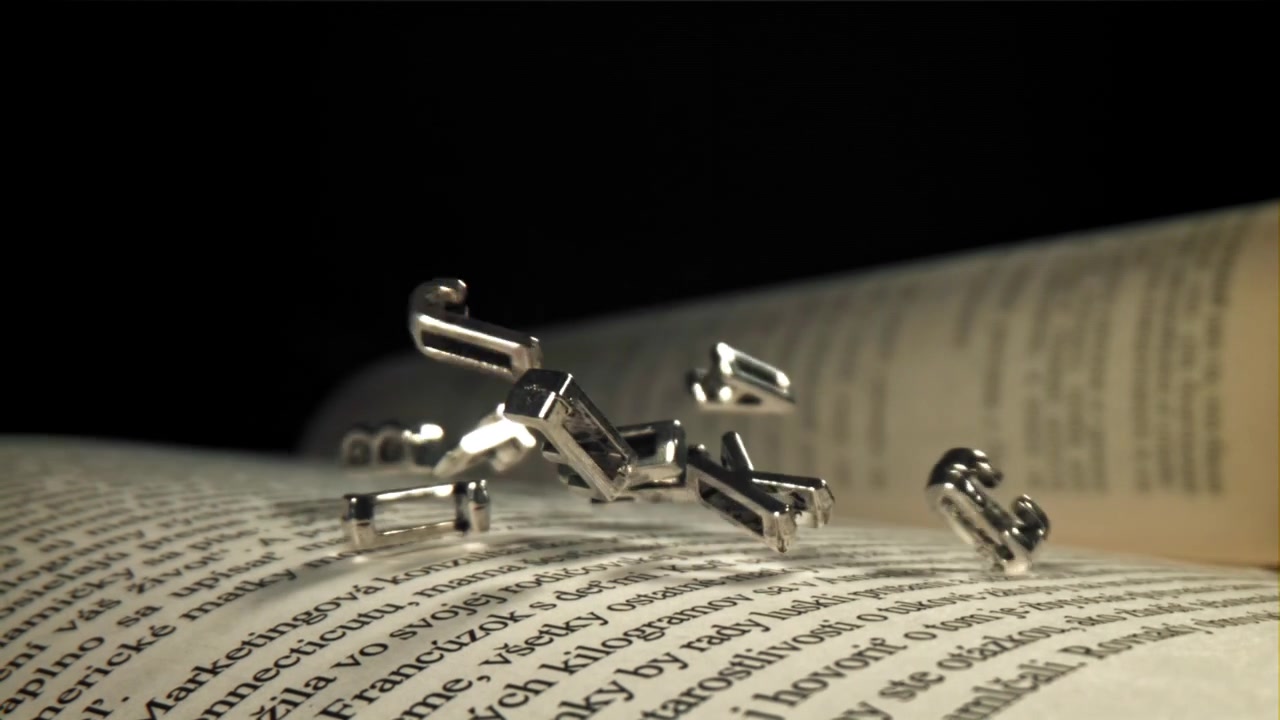 Lettere Metalliche che Cadono sulle Pagine di un Libro Aperto.