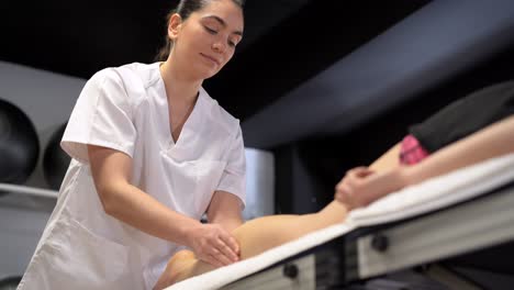 smiling female physiotherapist massaging leg of crop woman