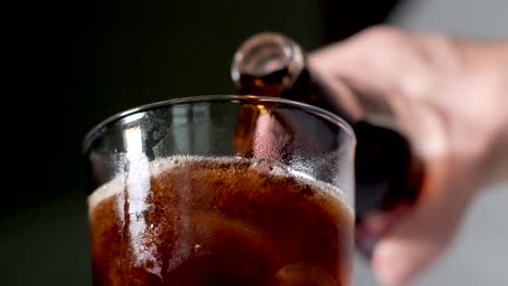 hand pouring coke or cola from a glass bottle into icy transparent drinking glass outdoors - closeup low angle view