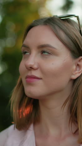 primer plano de una mujer joven mirando contemplativamente con gafas apoyadas en su cabeza, centrándose en algo por delante, con fondo de árboles y luz filtrándose a través de ellos