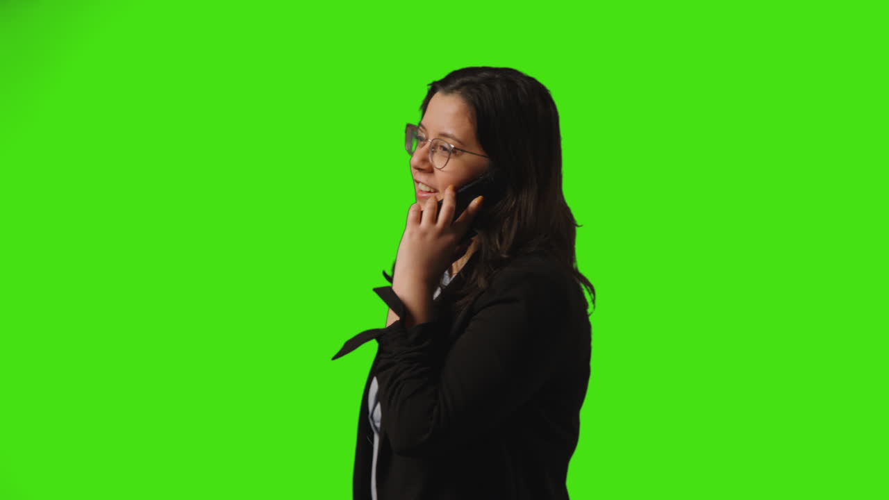 초록색 스크린 스튜디오 배경에 휴대전화로 이야기하는 안경을 입은 좌절한 젊은 사업가
